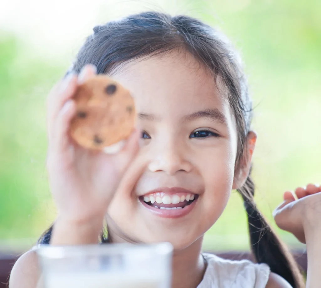 Cute asian little child girl smiling and holding cookie with milk for breakfast with happiness