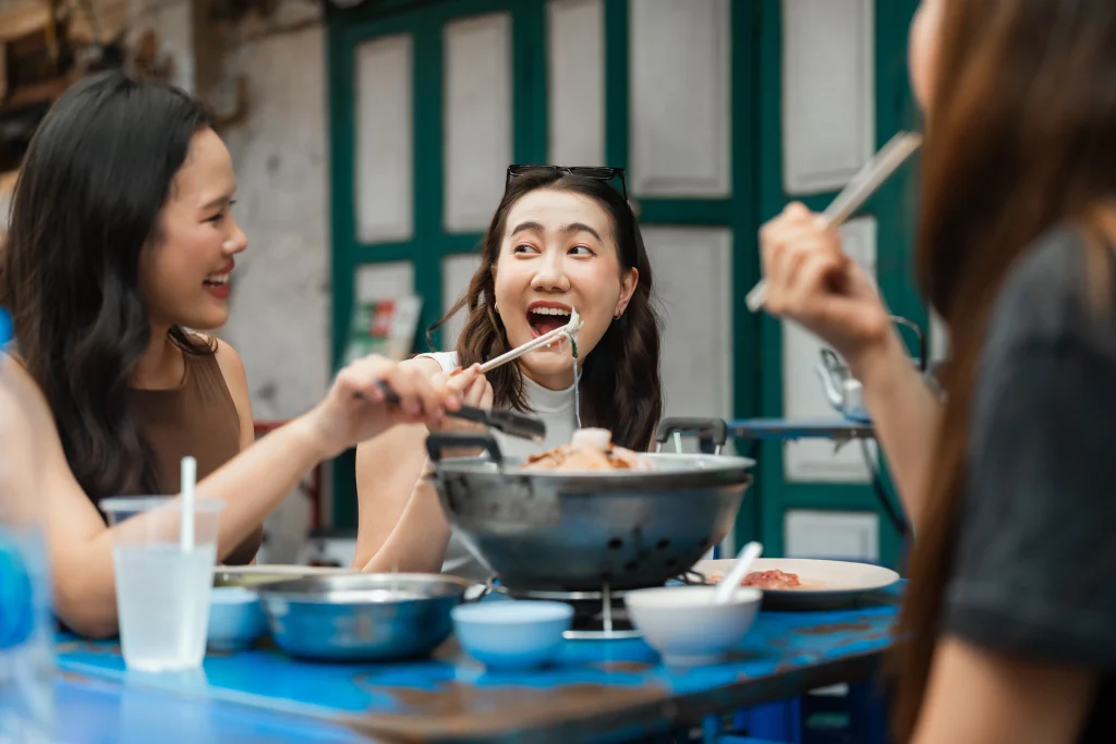 Group of asian friends eating noodles together at a street food market, using chopsticks and enjoying a delicious meal in a lively outdoor setting showing culture and lifestyle