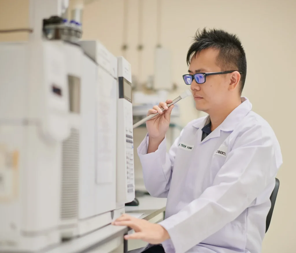Analytical chemist in a lab coat smelling aroma gas from a GCMS instrument.